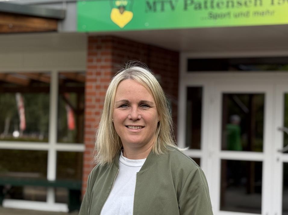 Frau mit blonden Haaren steht vor dem Eingang des MTV Pattensen 1909 e.V. mit gelbem Schild und Fenstern im Hintergrund.