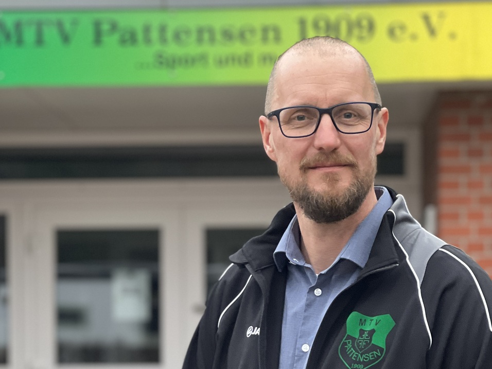 Mann mit Brille und Sportjacke steht vor dem Eingang des MTV Pattensen 1999 e.V. Vereinsgeb&auml;udes.
