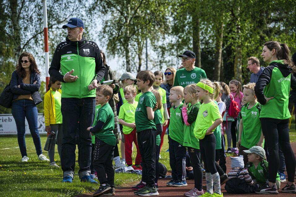 Gruppierung von Kindern in grünen Trikots bei einer Sportveranstaltung, umgeben von Trainern und Zuschauern.