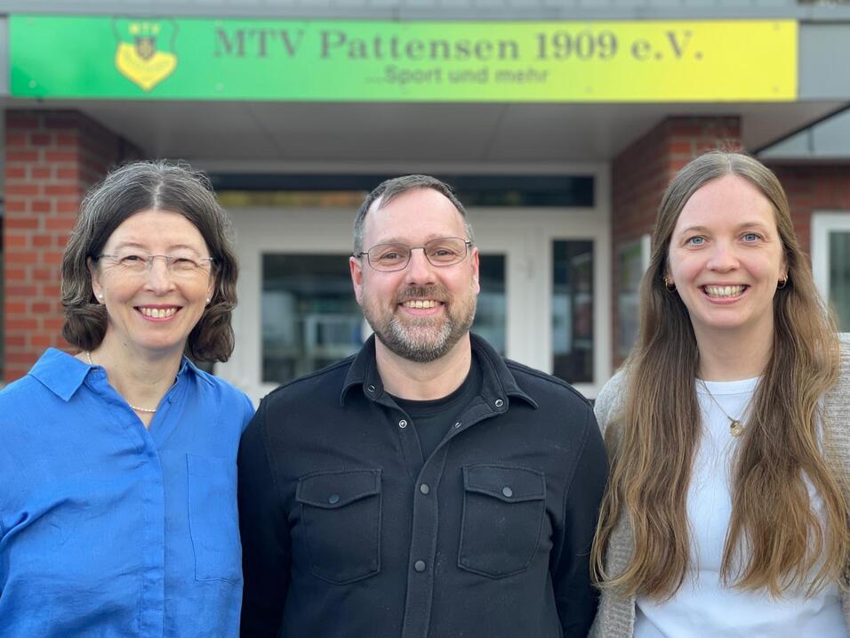 Drei Personen stehen vor dem Eingang des MTV Pattensen 1909 e.V. Gebäudes, lächelnd in casualer Kleidung.