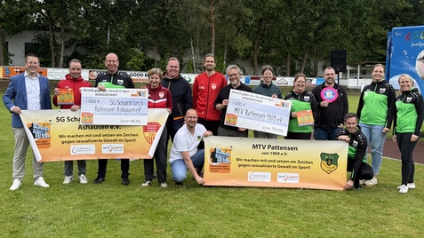Gruppe von Personen mit Schildern zur Spendenaktion f&uuml;r den Sport auf einem Platz im Freien, umgeben von B&auml;umen.