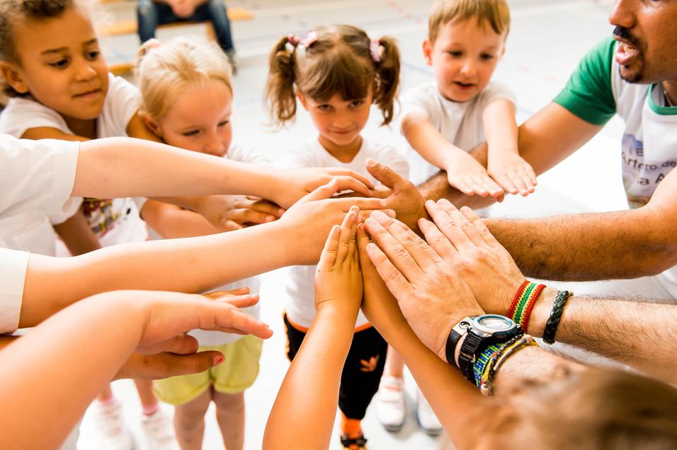 Kinder und Erwachsene legen ihre Hände in einem Kreis zusammen, symbolisieren Zusammenarbeit und Gemeinschaft.